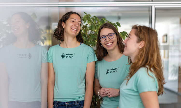 Three women in atom*innen shirts