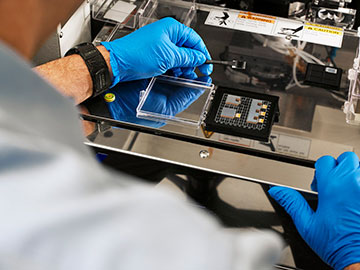 Hands in blue gloves holding an optics module