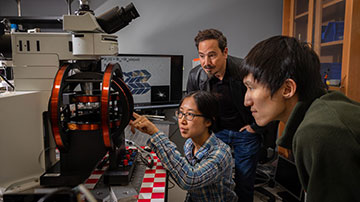 Three researchers sitting in a lab, looking at a machine