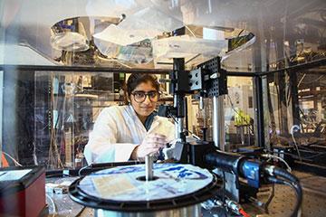 Researcher Manya Malhotra in a lab coat behind an experimental setup